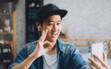 A young asian man making an ok gesture on his phone.