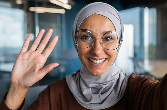 A woman wearing a hijab and glasses is waving her hand during her shopper mission.