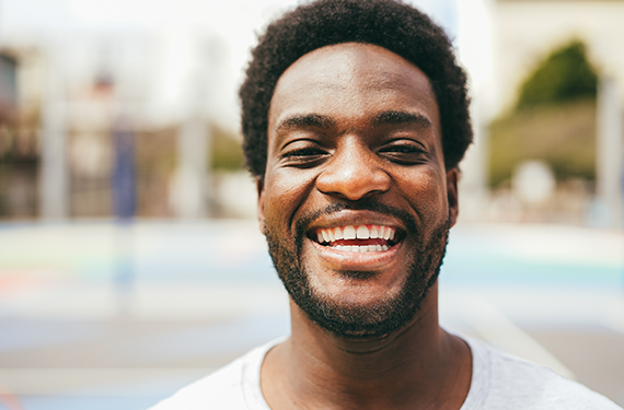 A creative black man smiling in front of a basketball court, testing solutions for success.